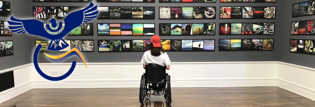 Une femme (vue de dos) au style branché, assise sur un fauteuil roulant, face à un mur de photos. Photo prise dans un musée de Berlin (Allemagne)