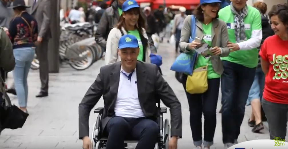Thomas Buberl (Directeur général d'AXA), souriant, se déplaçant en fauteuil roulant. D'autres membres de son équipe le suivent derrière